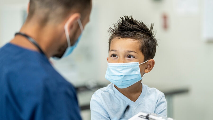 male doctor looking at and talking to little boy; both are wearing masks