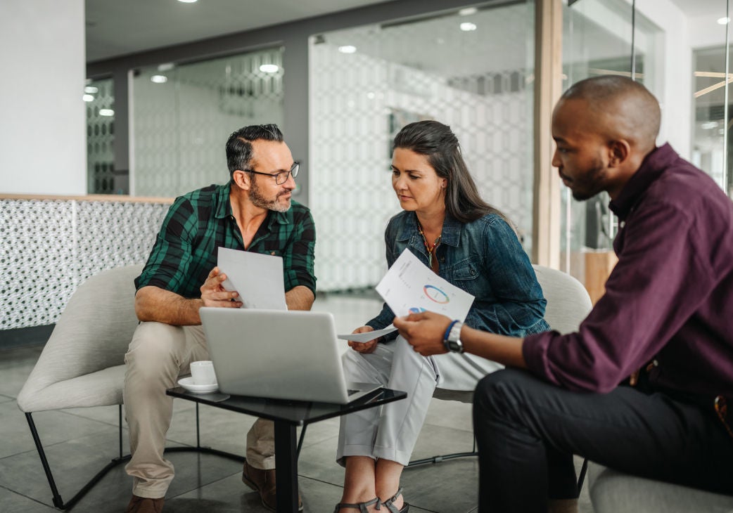 a group of people gathered around a laptop having a discussion and holding pamphlets of paper