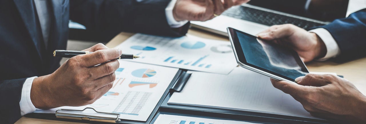 two people reviewing financial documents one with a pen the other an ipad in hand